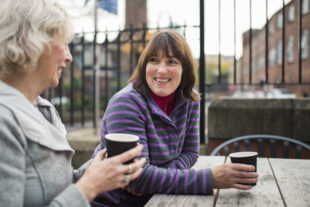 A mother and daughter sat having a conversation whilst drinking a coffee